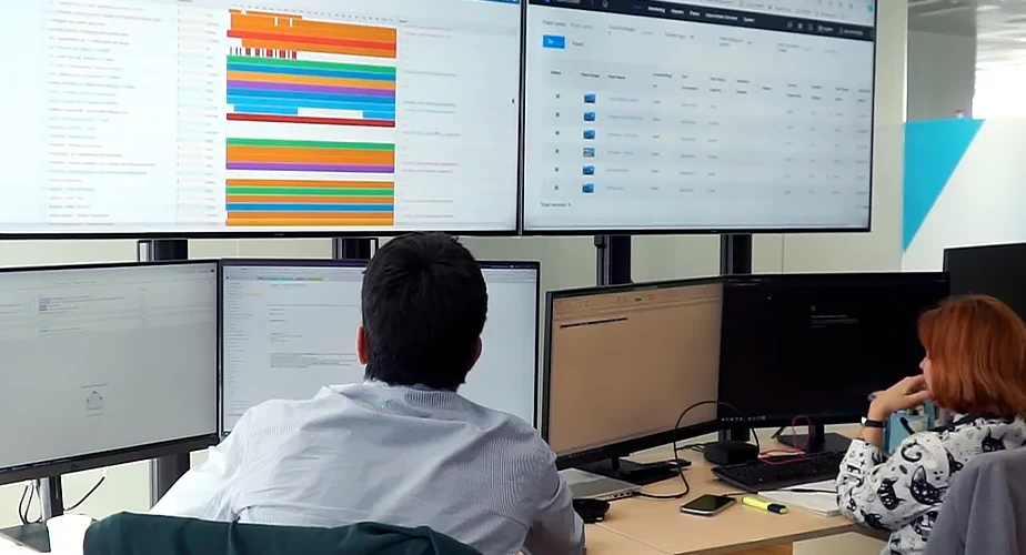 Two employees sit in front of several large screens and monitor environmental consumption (Photo)